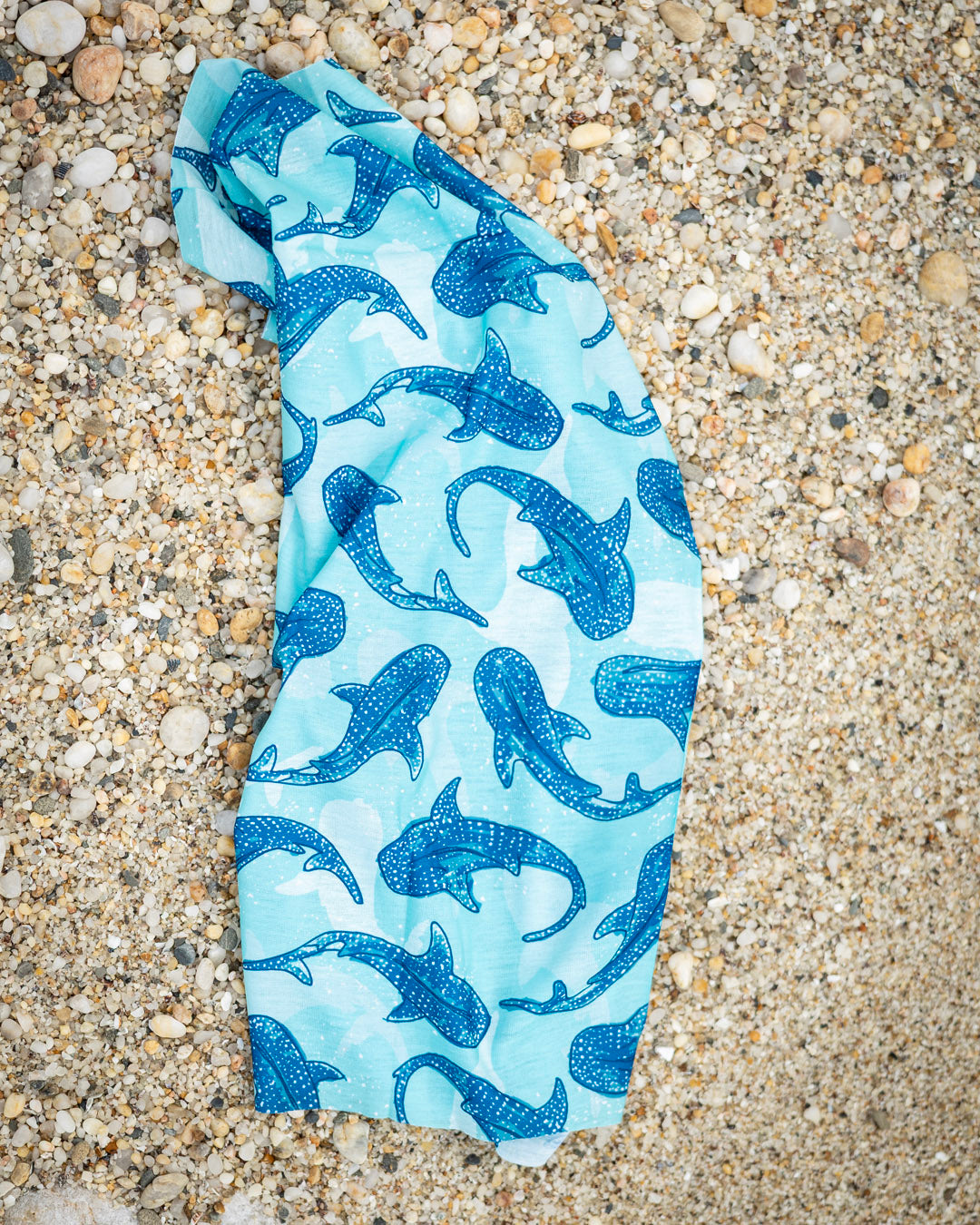 Blue neck gaiter / buff with whale shark pattern on a sandy beach