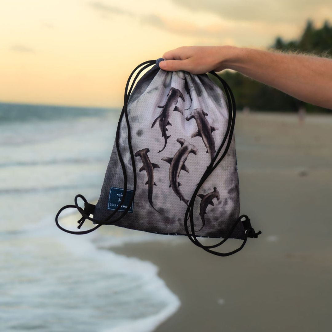 Close-up of a hand holding a Hammerhead Shark drawstring beach bag featuring multiple hammerhead shark illustrations
