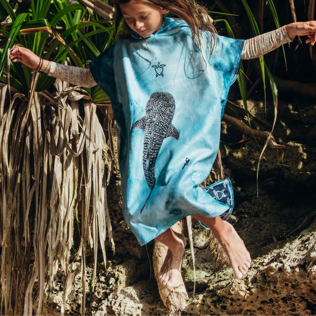 Female child wearing a blue Kids Whale Shark Changing Poncho Towel with a large whale shark illustration on the front.