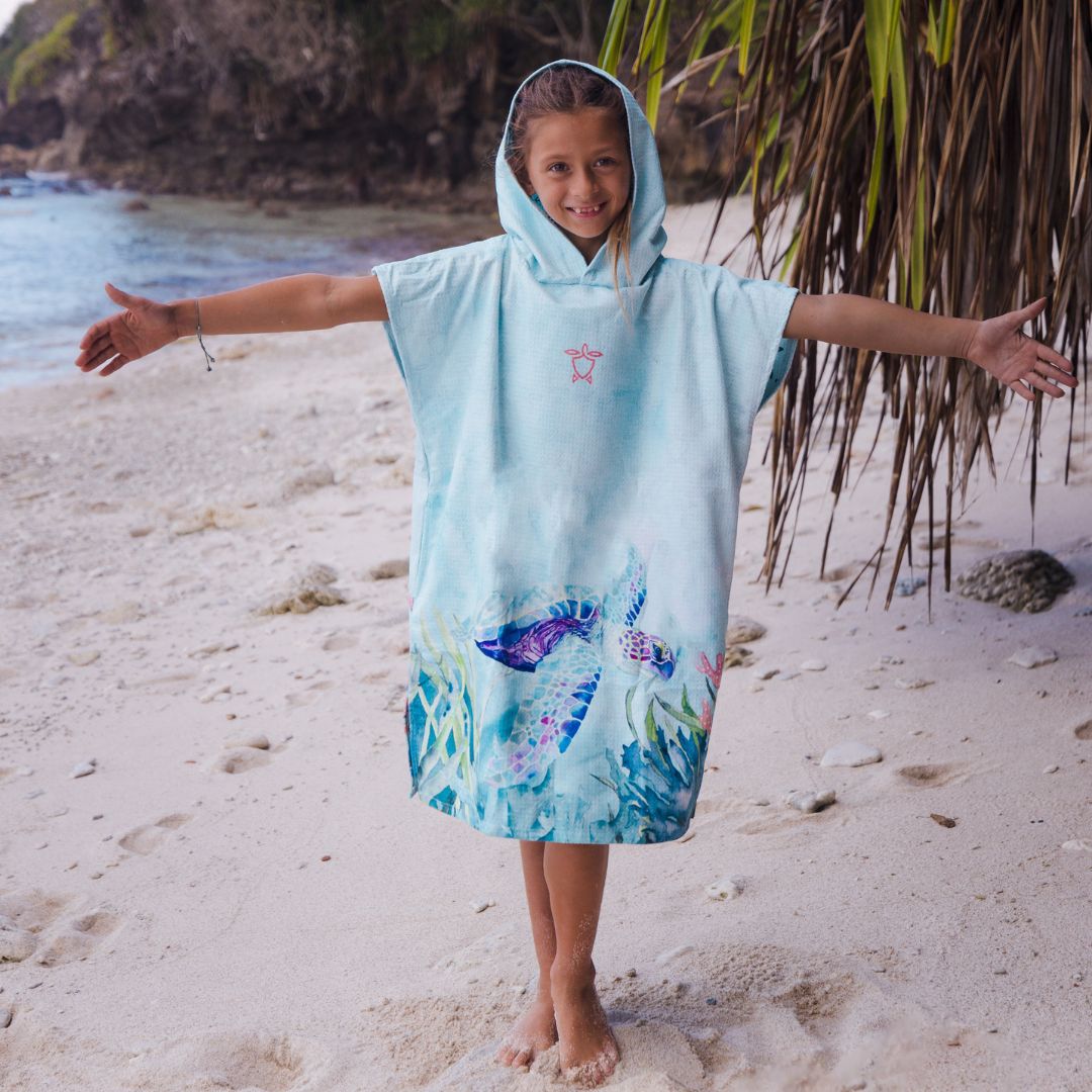 Child wearing a light blue hooded towel with a fish design on a sandy beach.