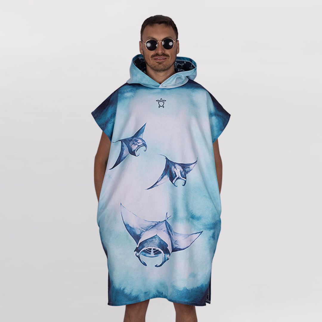 A man modeling a hooded poncho-style towel or cover-up with a blue and white manta ray print, set against a plain light gray studio background.