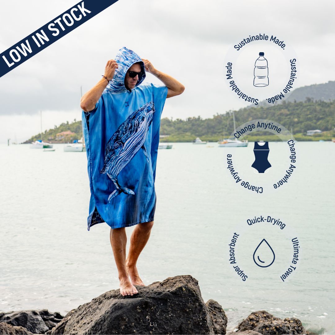 Person wearing the Humpback Whale Changing Poncho Towel with hood, featuring a large humpback whale design on the front. Icons indicate sustainable materials, quick-dry fabric, super absorbency, and a spacious fit for changing at the beach.