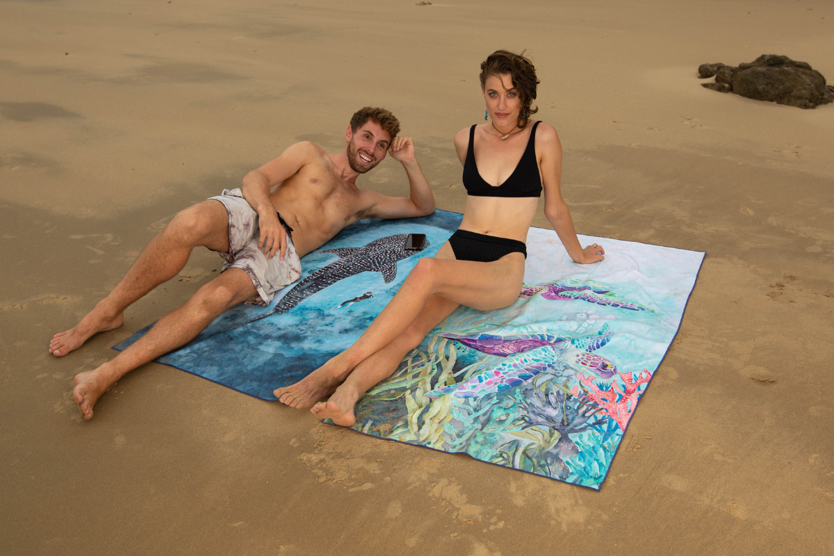 Models on the beach with turtle and whale shark beach towel designs