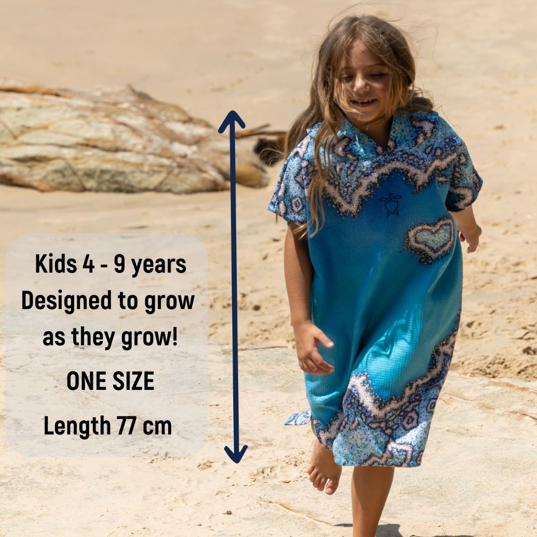 A young girl wearing a blue patterned beach cover-up dress walks on a sandy beach. Text on the left states 'Kids 4 - 9 years Designed to grow as they grow! ONE SIZE Length 77 cm' with a vertical measurement arrow overlaid.