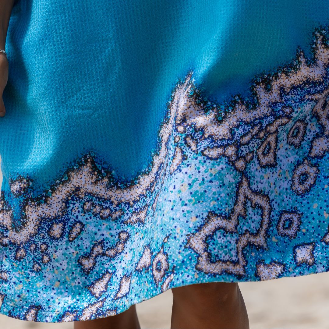 Close-up of a bright blue garment with a textured fabric and a wavy, speckled pattern in shades of blue, white, and black along the lower edge.