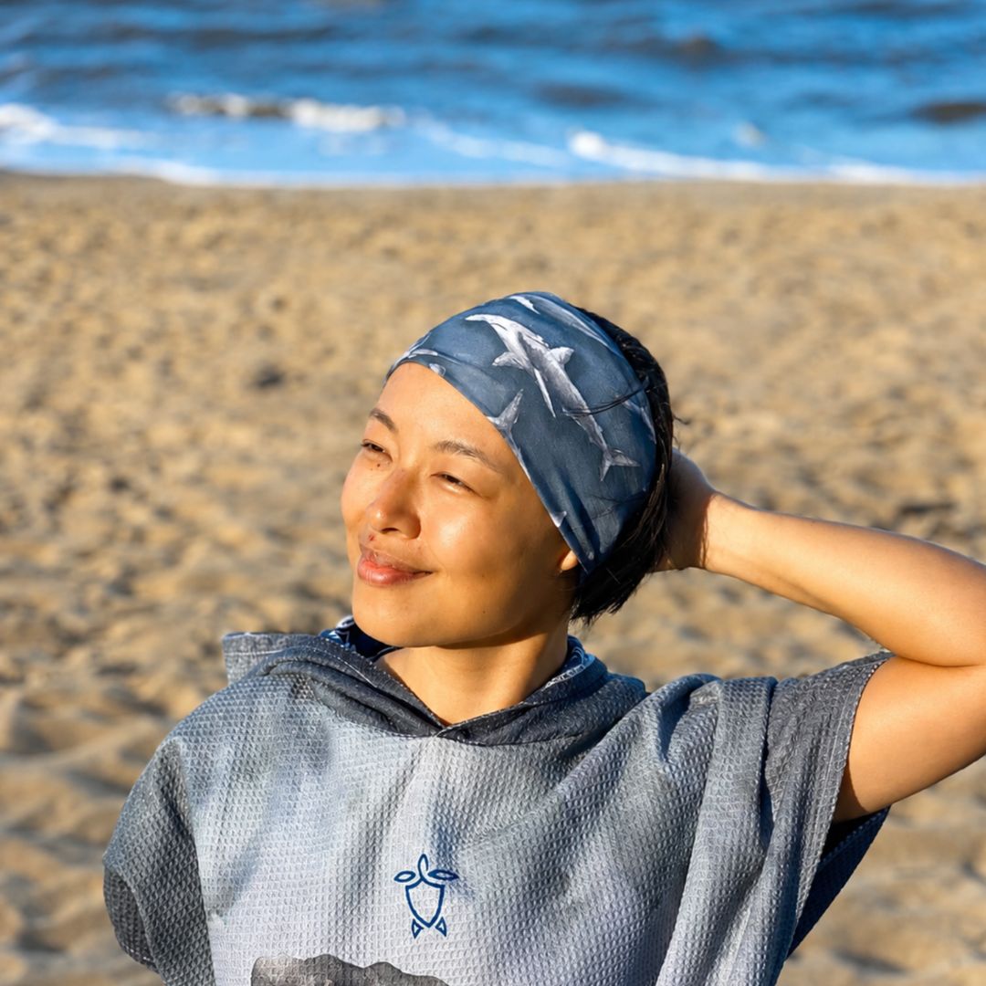 A woman on a sandy beach wearing a blue patterned swim headband 