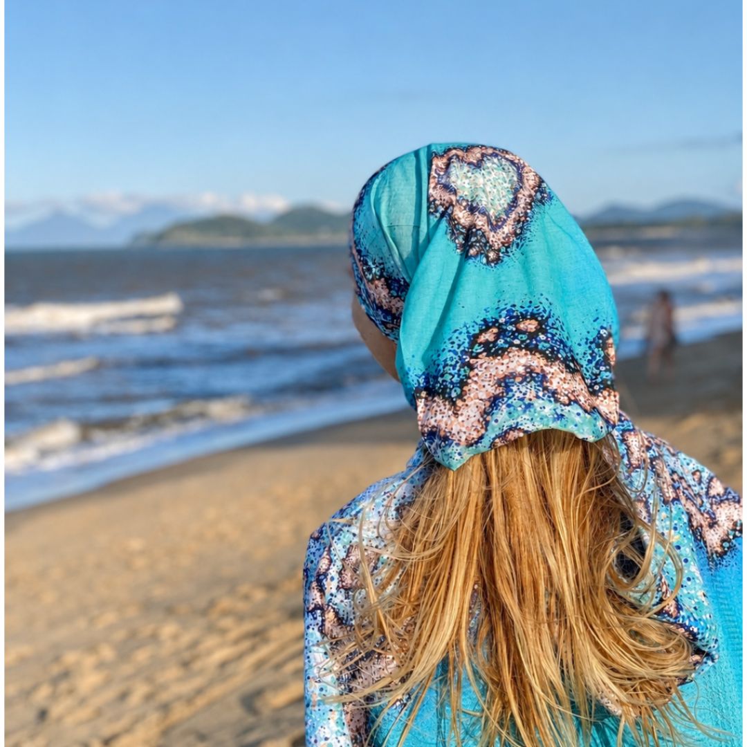 Person wearing a colorful hooded garment on a beach with ocean and sky in the background