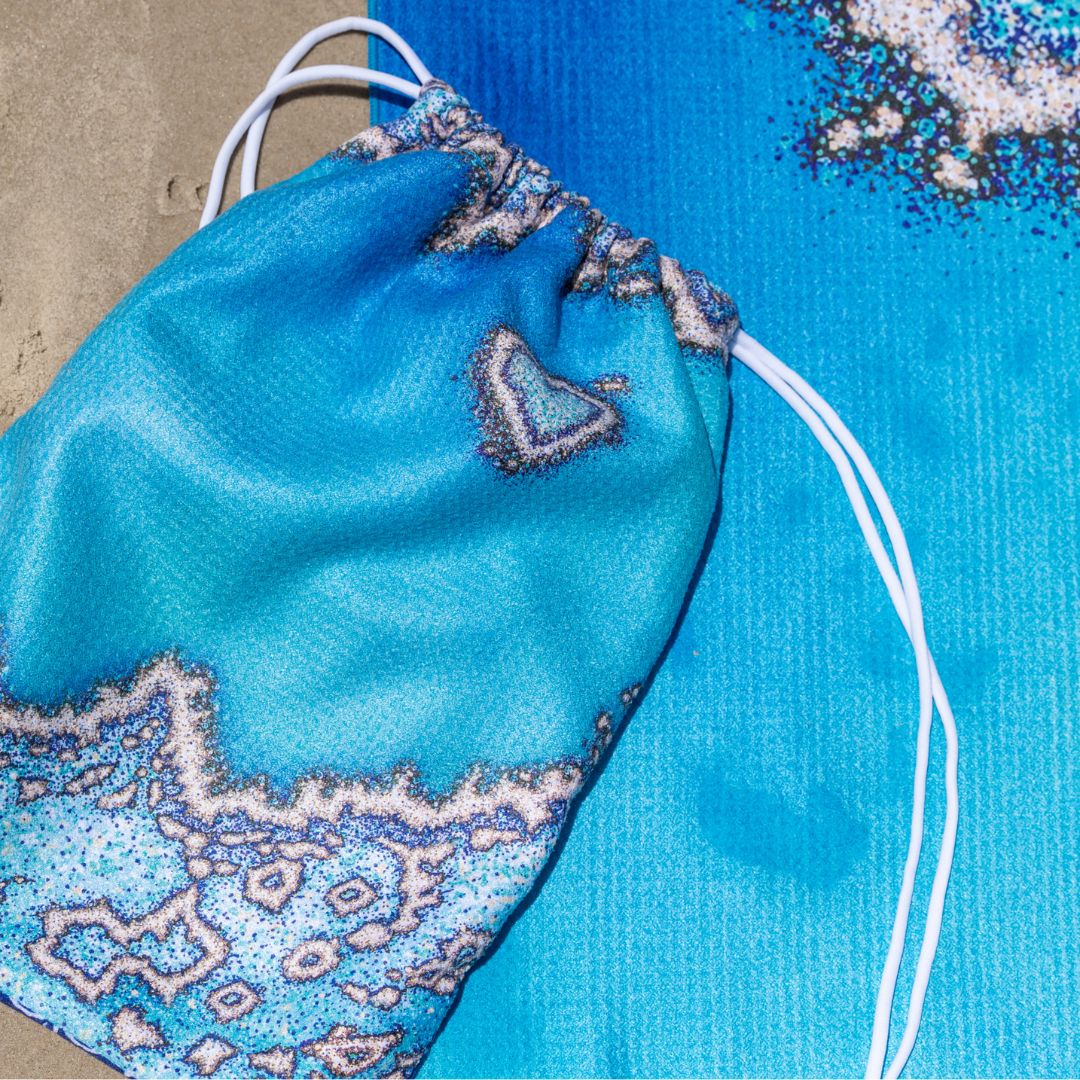 A close-up of a blue drawstring bag with a textured, patterned fabric and white drawstrings, placed on top of a matching blue textured surface.