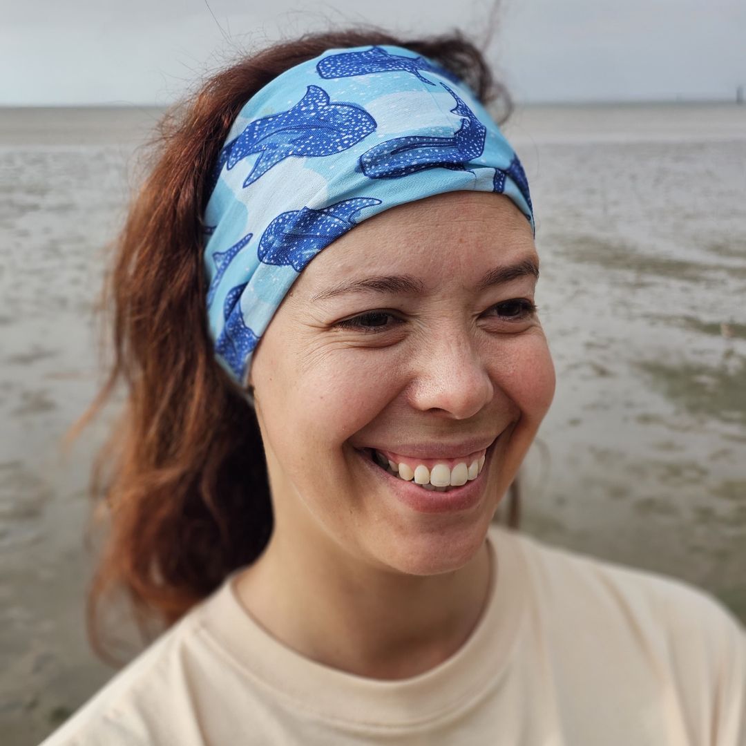 Close-up of a person wearing the Whale Shark Neck Gaiter as a headband with a blue whale shark print on a light blue background.